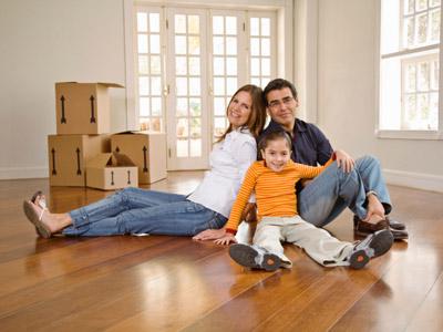 Smiling family sits on the floor of an empty house with moving boxes in background